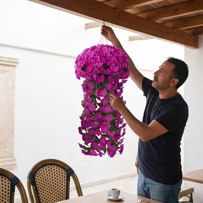 Un homme accroche la suspension magenta sous la pergola, près d'un café.